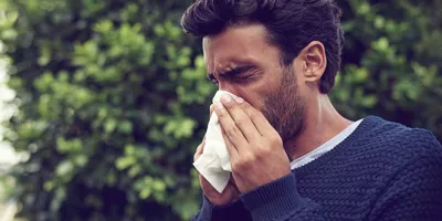 Un homme se mouche avec un mouchoir tout en ayant les  yeux larmoyants et le nez qui coule